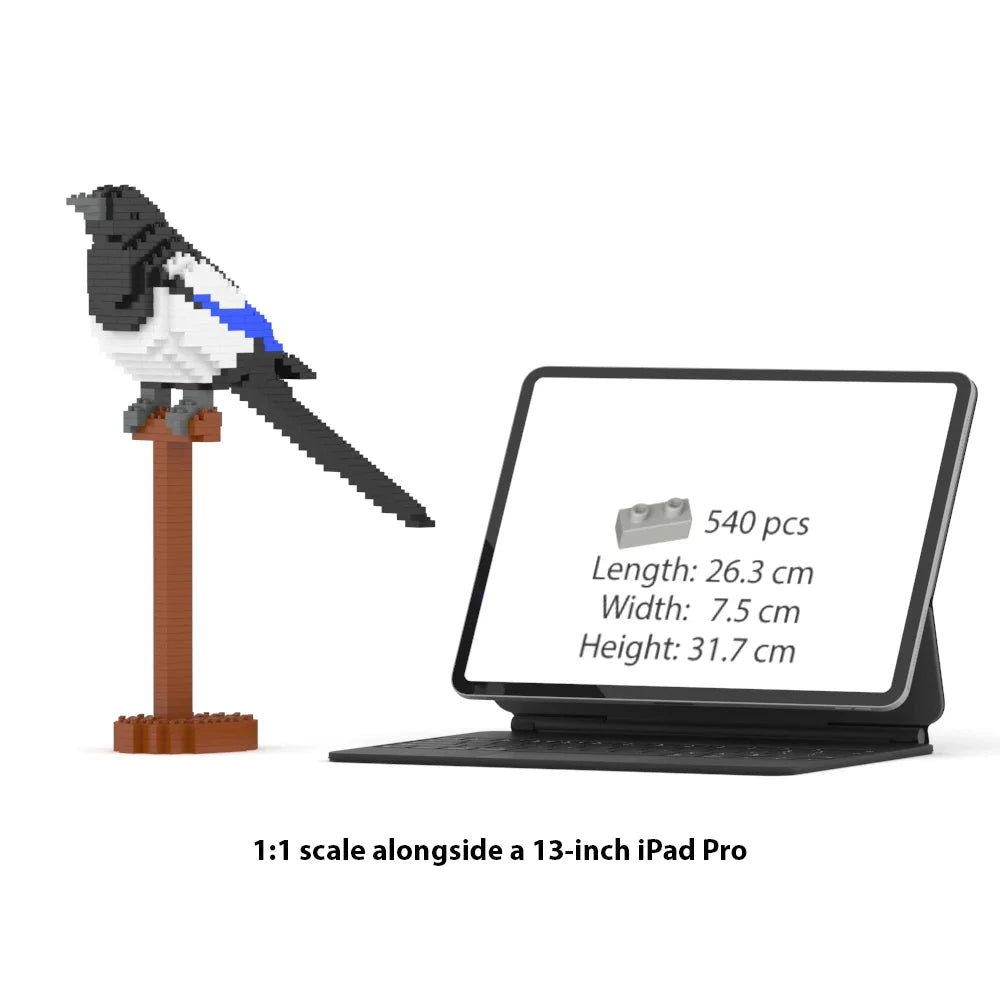 A 1:1 scale comparison showing a magpie bird block set on a brown stand beside a 13-inch iPad Pro. The magpie is built from small interlocking blocks and has a black head and tail, white body, and blue wing accents.