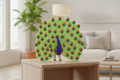 A colorful peacock sculpture made of interlocking building blocks stands on a light wood table in a bright, modern living room with a sofa, lamp, and potted plant in the background.