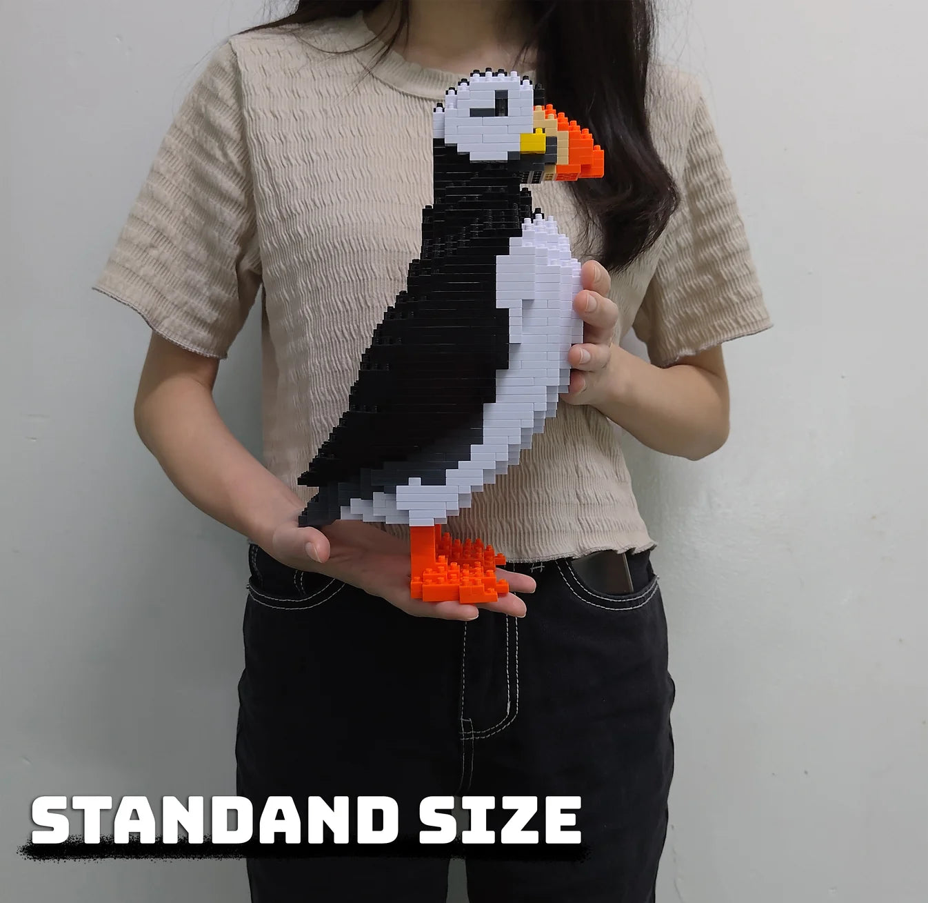 Person holding a pixelated puffin bird sculpture.