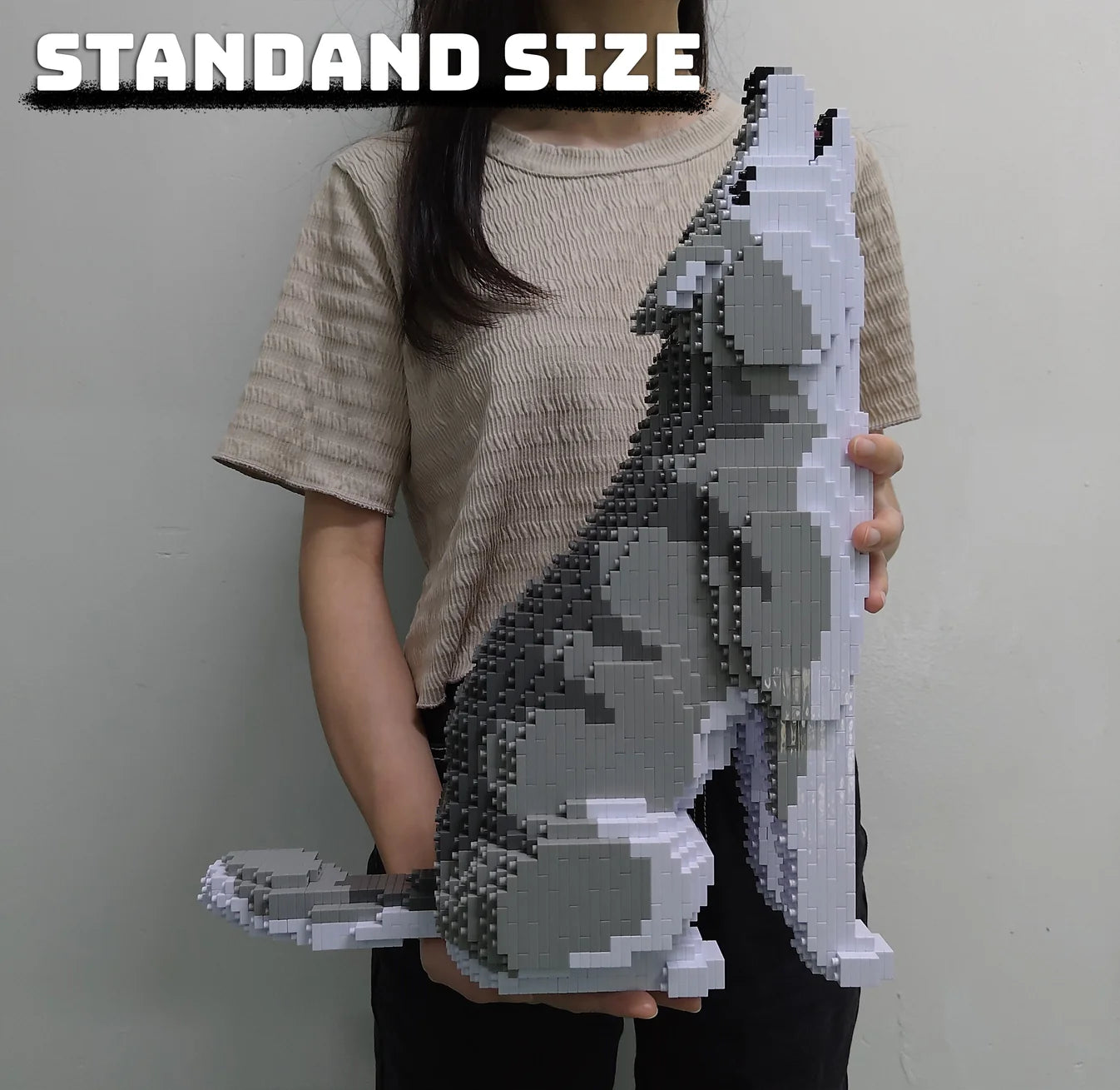Person holding a standard size gray and white wolf model made of interlocking bricks against a plain background.